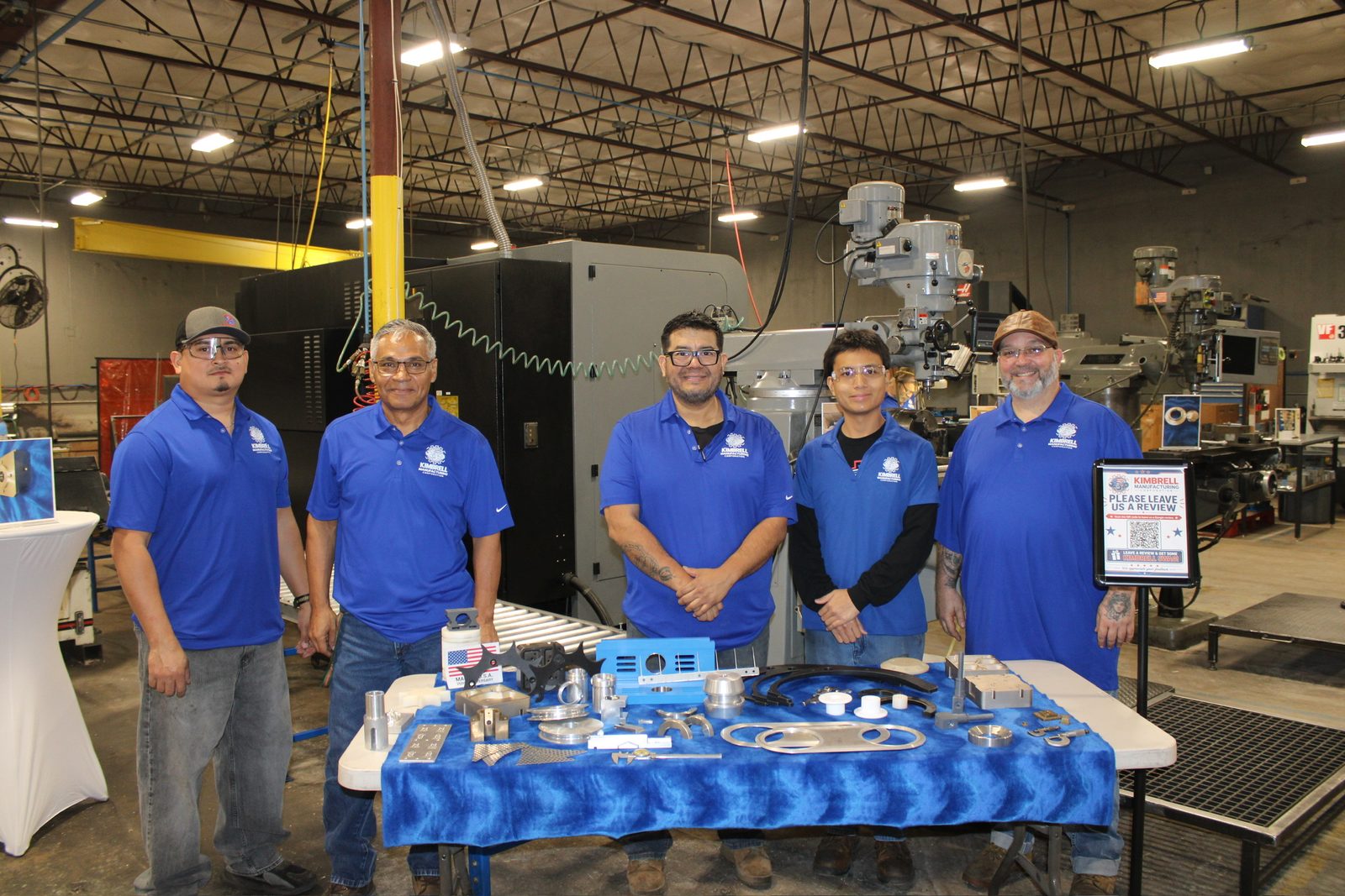 Five Kimbrell shop team members behind a table of machined and fabricated parts