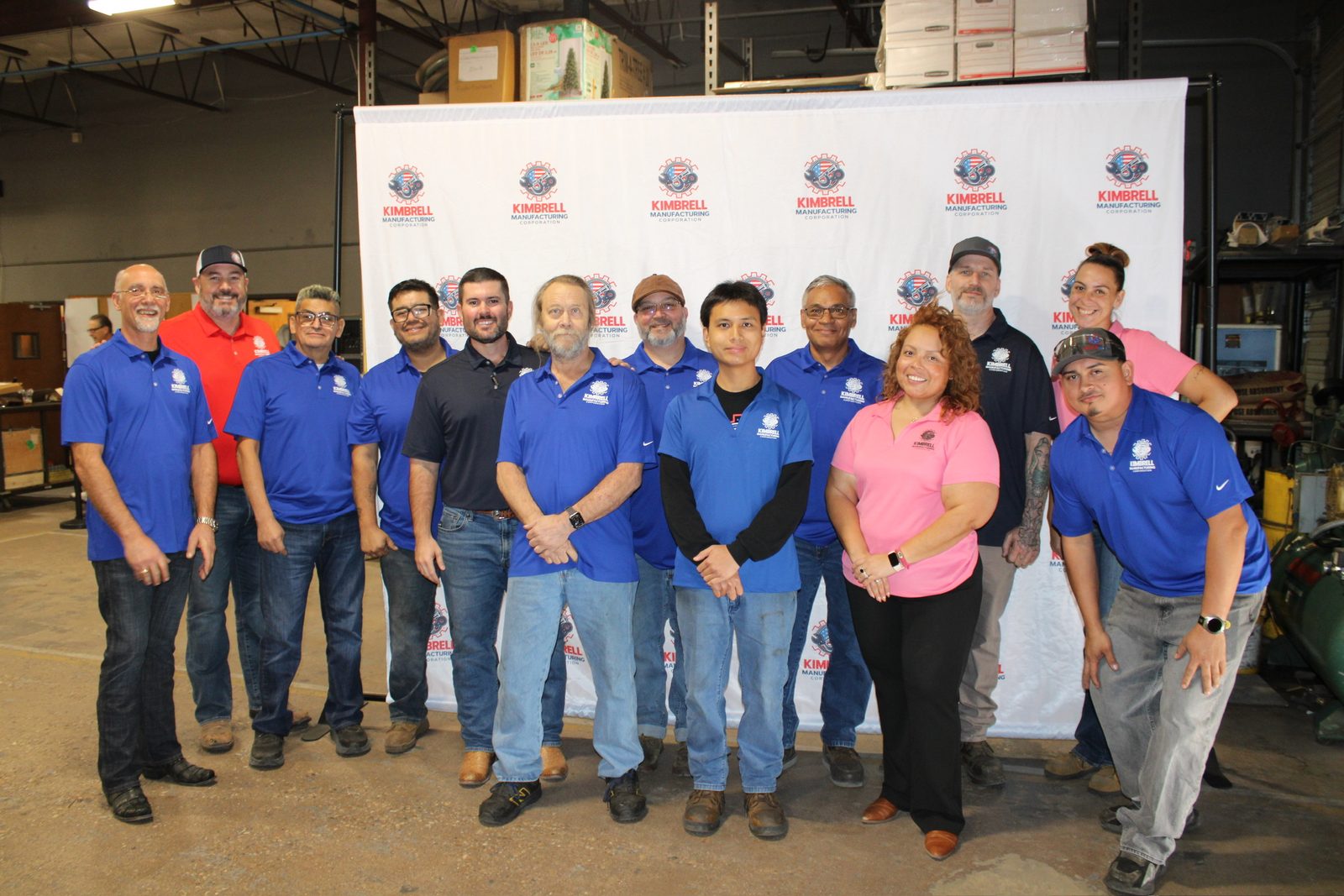 The Kimbrell Manufacturing Corporation team together in front of the company photo wall