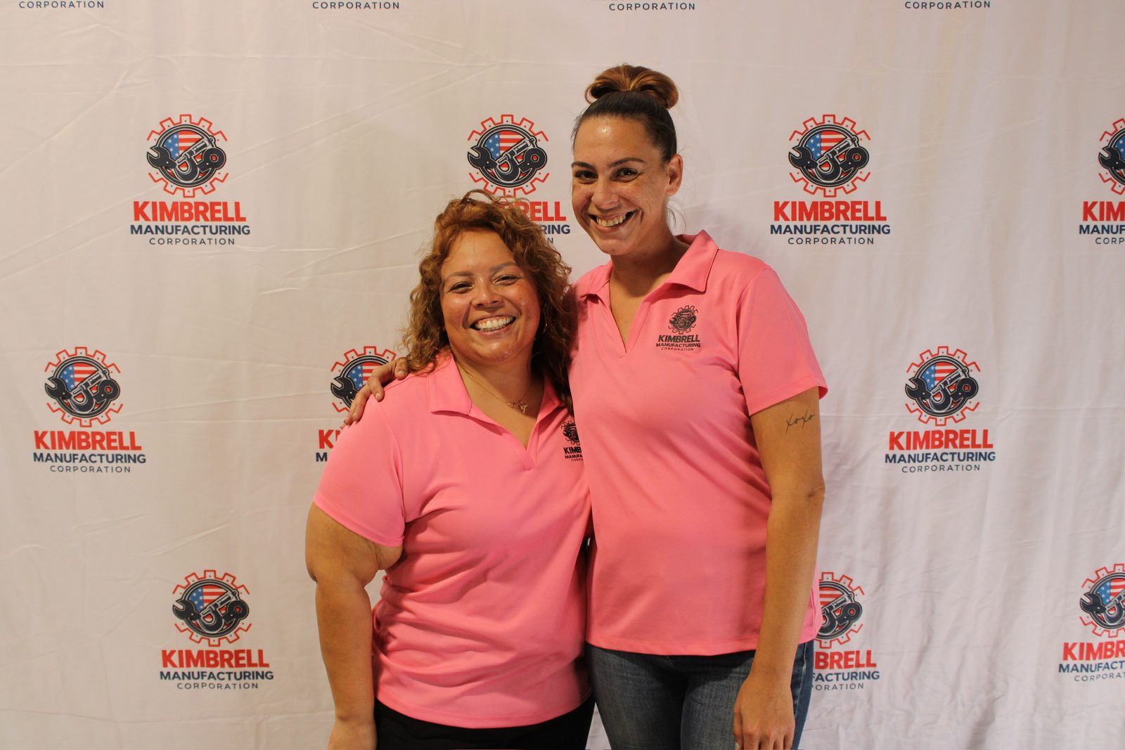 Two Kimbrell team members in pink company polos at the photo wall